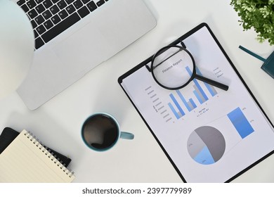 Top view laptop, magnifying glass and financial reports on white table - Powered by Shutterstock