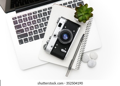 Top view of laptop and notepad with pan lying under vintage old camera and green flover over white background - Powered by Shutterstock