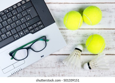 Top View Of Laptop, Sports Equipment, Tennis Ball, Shuttlecock And Glasses On The Sports Administration White Table.Business Concept.