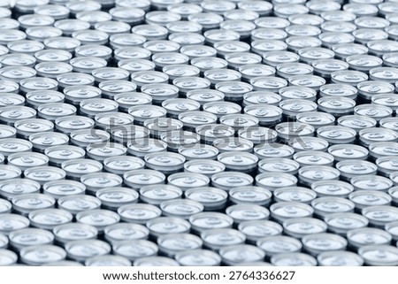 Top view of a large stack of aluminum beer cans arranged in rows, creating a repetitive metallic pattern. Concept of beverage production, brewery industry, packaging and mass manufacturing.