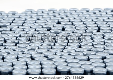 Top view of a large stack of aluminum beer cans arranged in rows, creating a repetitive metallic pattern. Concept of beverage production, brewery industry, packaging and mass manufacturing.