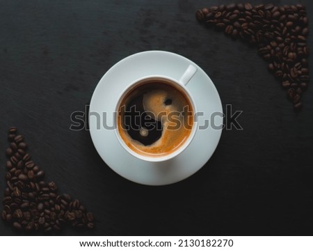 A top view of a latte art yin yang symbol in a white coffee cup on a black background