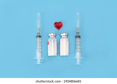 Top View. Layout On A Blue Background, Two Syringes, Two Bottles Of Vaccine, A Red Heart As A Sign Of Life And Health. Mass Vaccination. A Vital Necessity. Illustration For A Medical Article. Covid-19