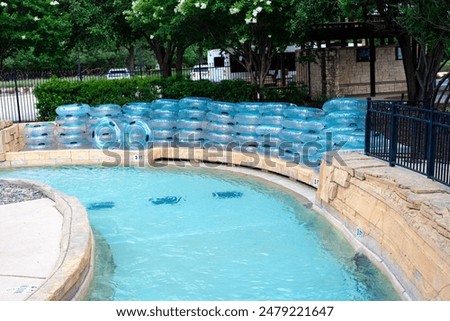 Top view lazy river full stack of clear floats transparent bathing swimming rings near metal fence entrance of upscale hotel resort waterpark in Grapevine, Texas, limestone wall overflow drainage. USA