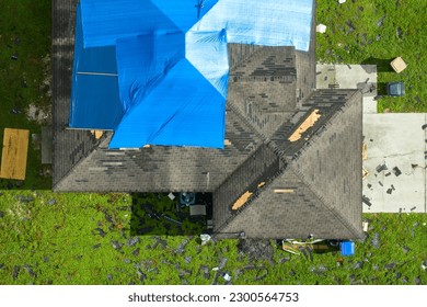 Top view of leaking house roof covered with protective tarp sheets against rain water leaks until replacement of asphalt shingles. Damage of building rooftop as aftermath of hurricane Ian in Florida