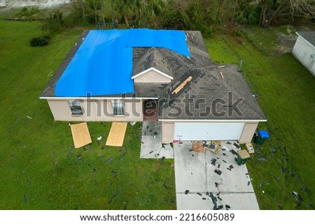 Top view of leaking house roof covered with protective tarp sheets against rain water leaks until replacement of asphalt shingles. Damage of building rooftop as aftermath of hurricane Ian in Florida