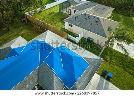 Top view of leaking house roof covered with protective tarp sheets against rain water leaks until replacement of asphalt shingles. Damage of building rooftop as aftermath of hurricane Ian in Florida