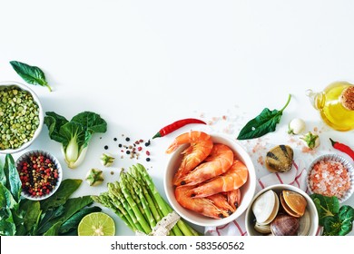 Top view of light dinner ingredients over white background with a copy space. Cooked prawns, clamps, asparagus, spinach, baby eggplant, brown rice, salt and pepper.