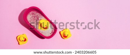 Top view little bath with rubber ducks on pink background. Wide banner. Copy space.