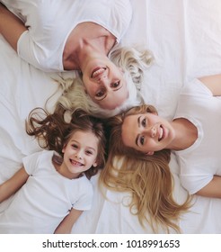 Top view of little girl, her attractive young mother and charming grandmother are lying on bed while spending time together at home. Women's generation. International Women's Day. Happy Mother's Day.