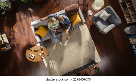 Top View Of Loft Apartment: Happy Couple Using Laptop In The Stylish Living Room. Looking At Digital Display. On Couch: Boyfriend Hugs Girlfriend, She Uses Computer For Online Shopping, E-business.