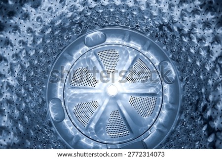 Top view look inside a stainless steel washing machine drum with a circular silver pulsator and bright light reflections