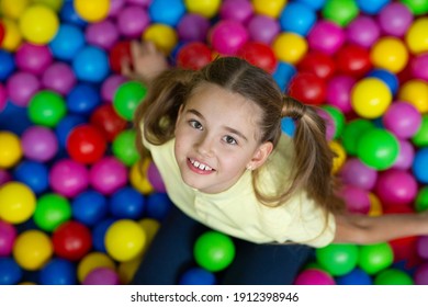 Top View Of Lovely Teenage Girl Sitting At Ball Pond In Amusement Centre. Overhead Shot Of Adolescent Child Having Fun At Kids Playground. Fun Weekend Activities Concept