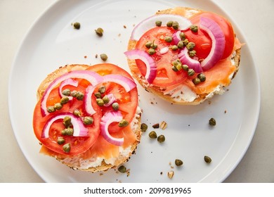 Top View of Lox, Tomatoes, Capers, Red Onion, and Cream Cheese on Bagel on White Plate