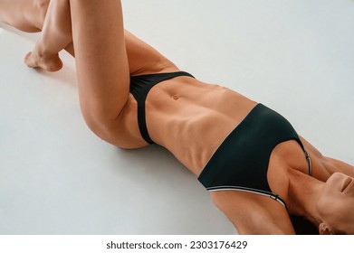 Top view, lying down on the floor. Young caucasian woman with athletic body shape is indoors at daytime.