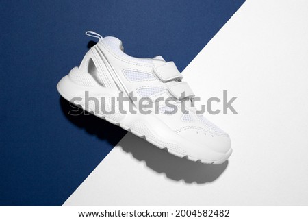 top view macro one piece white girly running shoes on the side with velcro fasteners for easy shoeing on a modern blue and white paper background with hard light.