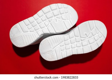 top view macro raised sole with treads on white running shoes with hard shadows isolated on a red background, sneakers with soles up.
