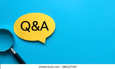 Top view of magnifying glass and yellow speech bubble written with QNA Question and Answer on blue background with copy space.