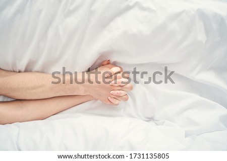 Top view of the male and female hands with intertwined fingers lying on the bed