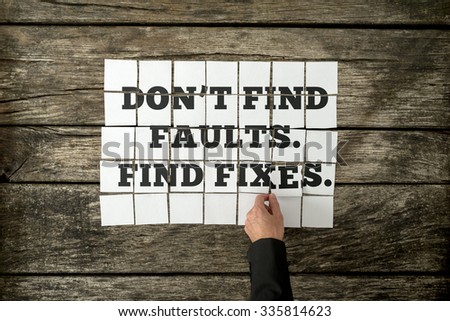 Top view of male hand assembling a Don't find faults. Find fixes sign with white cards over a textured rustic wooden boards.