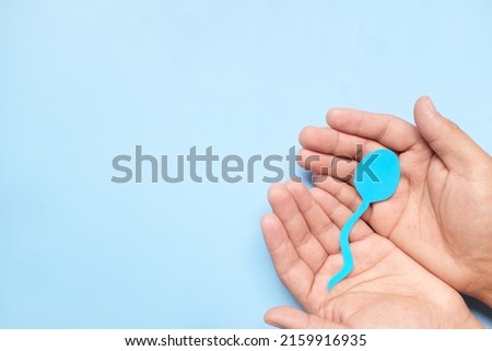 Top view of male hand holding sperm cutout in blue background. Men's health, sperm donation and care concept. 