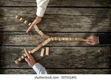 Top View Of Male Hand Pushing Dominos Placed In Y Shape Knocking Them Down And Two Other Hands Stopping Them Each On One Side. Conceptual Of Crisis Management In Business.