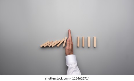 Top View Of Male Hand In White Shirt Stopping Falling Dominos On Gray Desk.