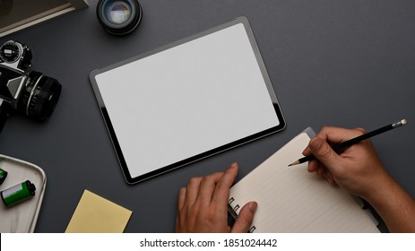 Top view of male hand writing on notebook on workspace with tablet and supplies, include clipping path
