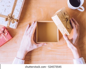 Top View Of Male Hands Opening Gift Box, Coffee Cup On Wooden Table.