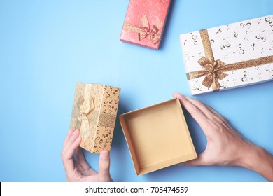 Top View Of Male Hands Opening A Gift Box, Presents On Blue Background.