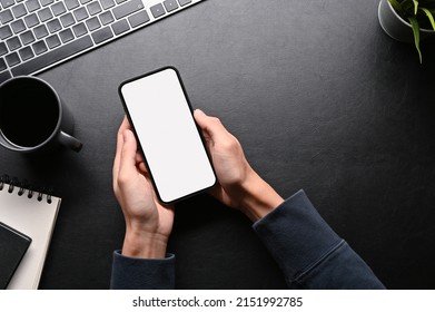 Top view, A male hands using cellphone on his dark stylish workspace table. top view, phone white screen mockup. - Powered by Shutterstock