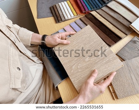 Top view: male interior designer chooses finishes for a house, examines samples of wood and fabrics. Concept: the architect selects the color of textiles and samples of materials for furniture
