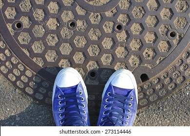 Top view of male sneakers on round steel sewer manhole on pavement in Japan.