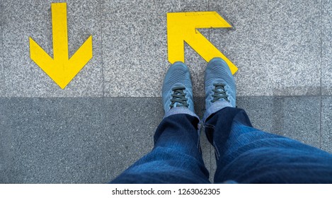 Top View Of Man Feet Standing Over Arrow Symbol On Subway Platform. Yellow Arrow Sign On Floor At The Train Station.