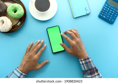 top view of man hand using smart phone with donuts, tea blue background 