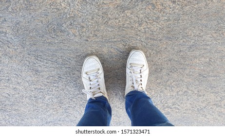 Top View Of A Man Legs Wearing Jeans And White Sneakers Standing On The Stone Tile Floor.