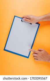 Top view man pointing to clipboard while holding it on orange background. vertical