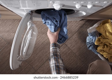 Top view of a man putting dirty clothes into the washing machine. Built-in household appliances in the home kitchen.