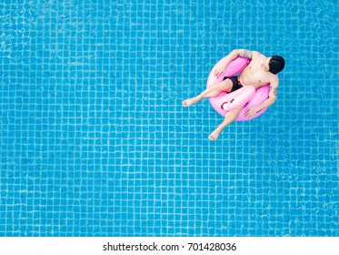 Top View, A Man Relaxing On Pink Flamingo Swim Pool Float, On Swimming Pool In Summer