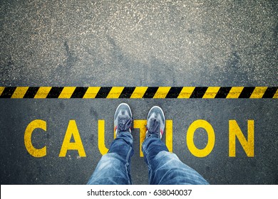 Top View Of A Man Stands On Industrial Striped Asphalt Floor With Warning Yellow Black Caution Pattern.