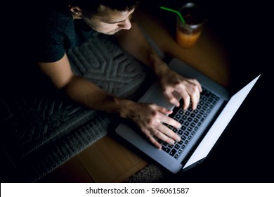 Top View Of Man Typing Messages On Laptop Keyboard, Lying On Carpet In Dark Room