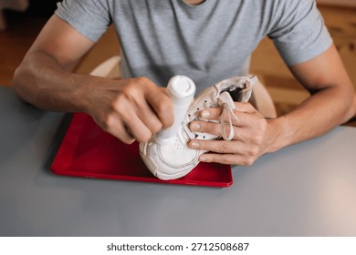 Top view of man using bottle of shoe whitener and painting scuffed surface of dirty white sneaker, illustrating process of cleaning, recoloring, and restoring footwear.