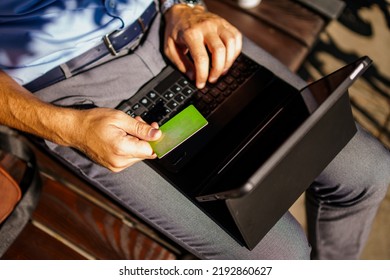 Top View Of Man Using Credit Card For Online Shopping Outdoor While Sitting On Bench.