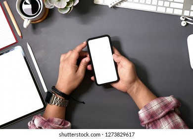 Top view man using a mobile smartphone over a workspace desk that has blank mockup screen.