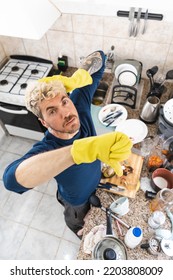 Top View Of Man Wearing Cleaning Gloves With Thumbs Down Because Of His Messy Kitchen. Vertical Photo