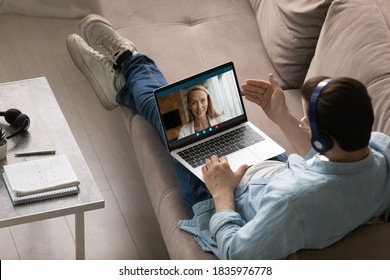 Top view man wearing headphones chatting with woman online, sitting on couch with laptop on laps, enjoying leisure time, boyfriend talking with girlfriend by video call, using social media app - Shutterstock ID 1835976778