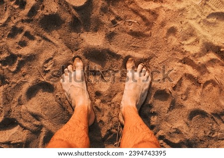 Top view of man's bare feet standing on the sand at the beach at sunset. The concept of vacation at sea, summer travel.