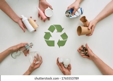Top view of many hands holding different waste, garbage types with recycling sign made of paper in the center over white background. Sorting, recycling waste concept. Horizontal shot. Top view