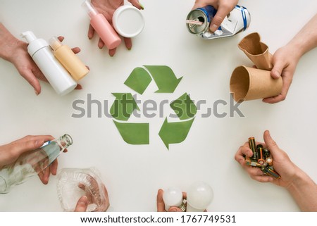 Top view of many hands holding different waste, garbage types with recycling sign made of paper in the center over white background. Sorting, recycling waste concept. Horizontal shot. Top view