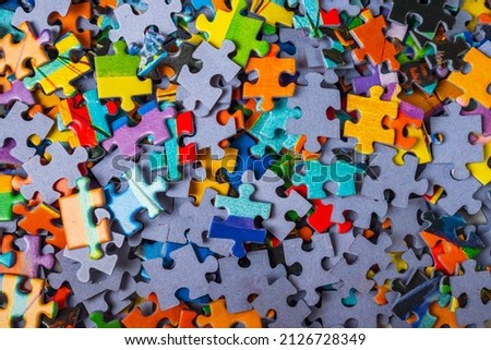 Top view many jigsaw puzzle pieces over the entire frame. A background image of scattered colorful puzzle pieces
